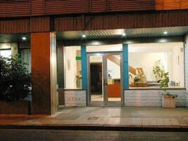 Un edificio con entrada de vidrio, fachada de madera y un pequeño espacio al aire libre con plantas.