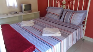 A bed with striped bedding, a television on a shelf, and a red wall. - Casa da Maisa (Porto Seguro)