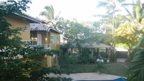 A yellow building with a tiled roof, surrounded by lush greenery and a swimming pool. - Casa da Maisa (Porto Seguro)