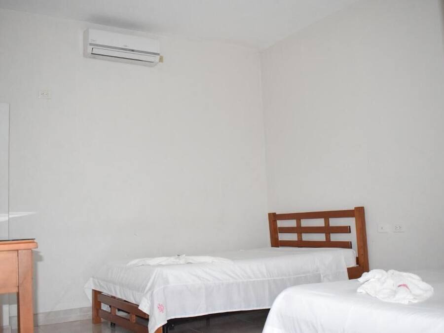 Una habitación pequeña y limpia con una cama individual, cabecero de madera, una mesita y un equipo de aire acondicionado instalado en la pared.