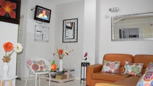 A living room with a white chair, an orange sofa, a TV, and a mirror. - Hotel Orquídea Neiva (Neiva)