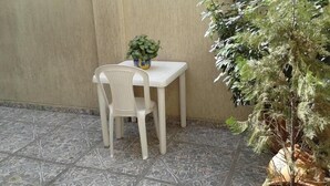 A small outdoor seating area with a white plastic chair and table, a potted plant on the table, and a large potted plant to the right. - Hotel Orquídea Neiva (Neiva)
