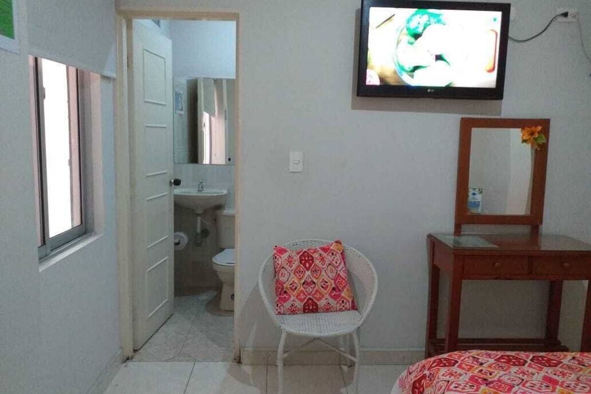 A room with a bed, a television mounted on the wall, a mirror, a chair, and a door leading to a bathroom.