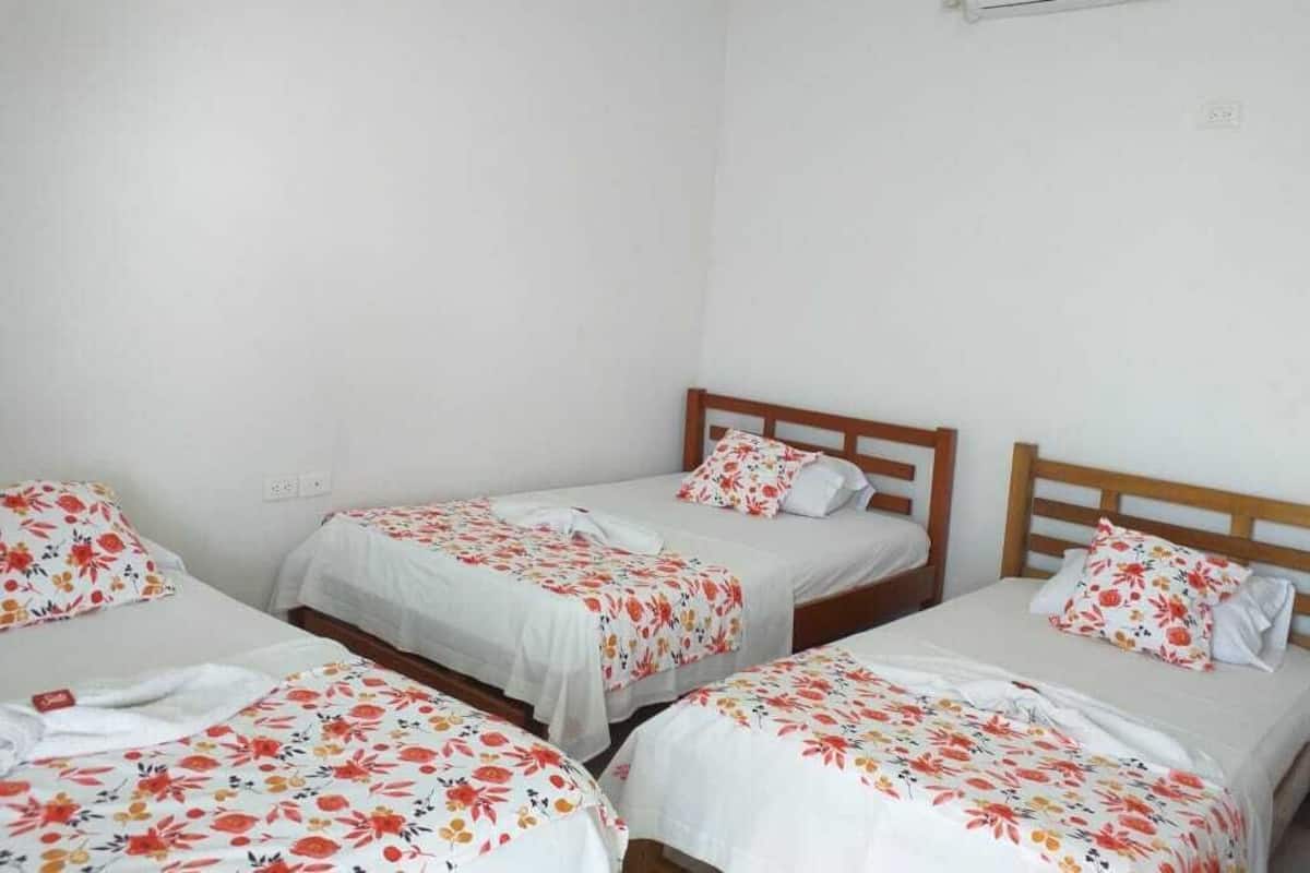 A room with four single beds, each with a wooden headboard and white bedding with a floral pattern.