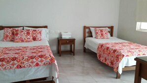 A hotel room with two beds, each with patterned bedding and pillows, a small wooden nightstand, and a window providing natural light. - Hotel Orquídea Neiva (Neiva)