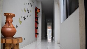 A hallway with a tiled floor, a large vase on a wooden stool, and a life preserver hanging on the wall. - Hotel Orquídea Neiva (Neiva)