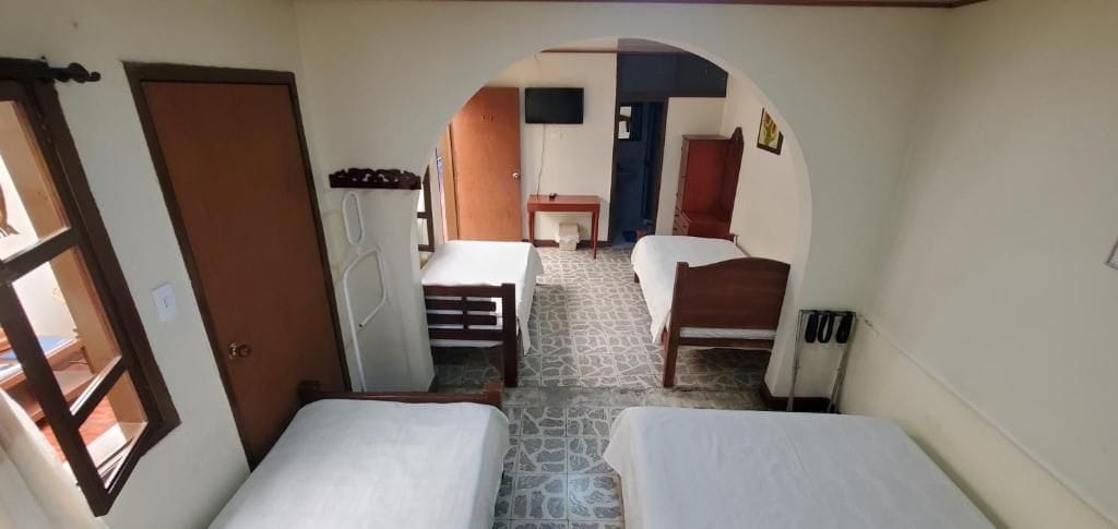 Una habitación con dos camas, un escritorio, una silla, un televisor y una puerta que da a otra estancia.