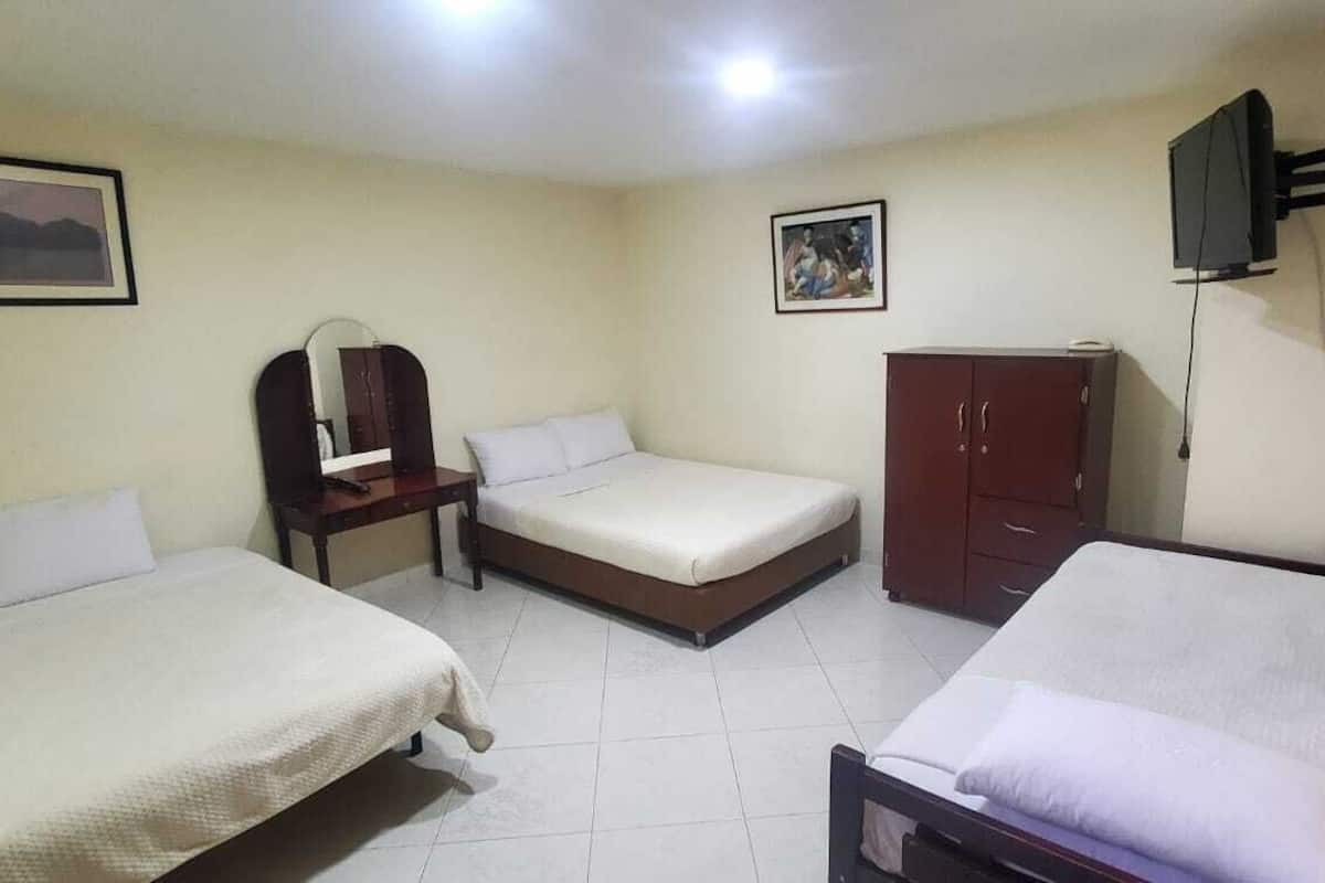 A hotel room with three beds, a wardrobe, a desk, and a television.