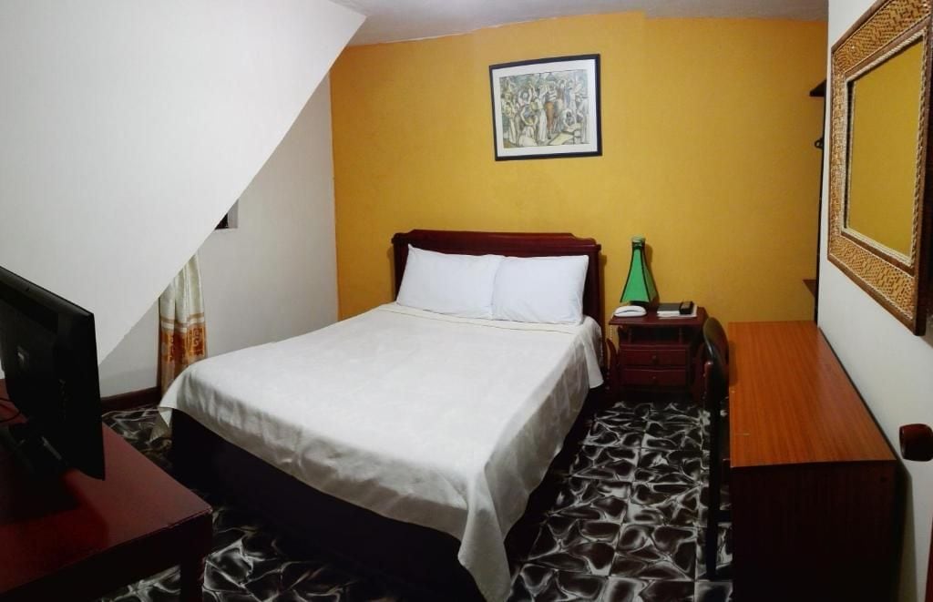 Een hotelkamer met een bed, nachtkastje, lamp en een spiegel aan de muur.