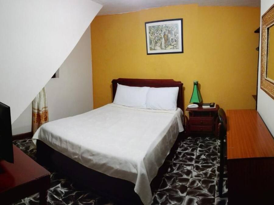 A hotel room with a bed, bedside table, lamp, and a mirror on the wall.