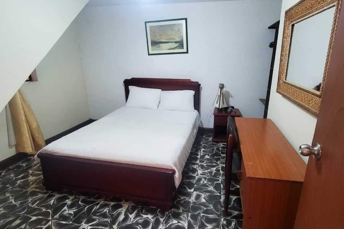 A bedroom with a bed, a nightstand, a bedside table, a mirror, and a picture on the wall.