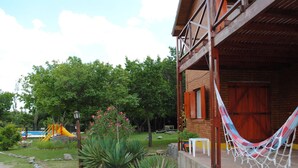 A wooden cabin with a hammock, a play area, and a garden with large plants. - Apart Hotel Camino del Cerro (Merlo)