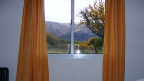 A bedroom with a bed, curtains, and a window with a mountain view. - Apart Hotel Camino del Cerro (Merlo)