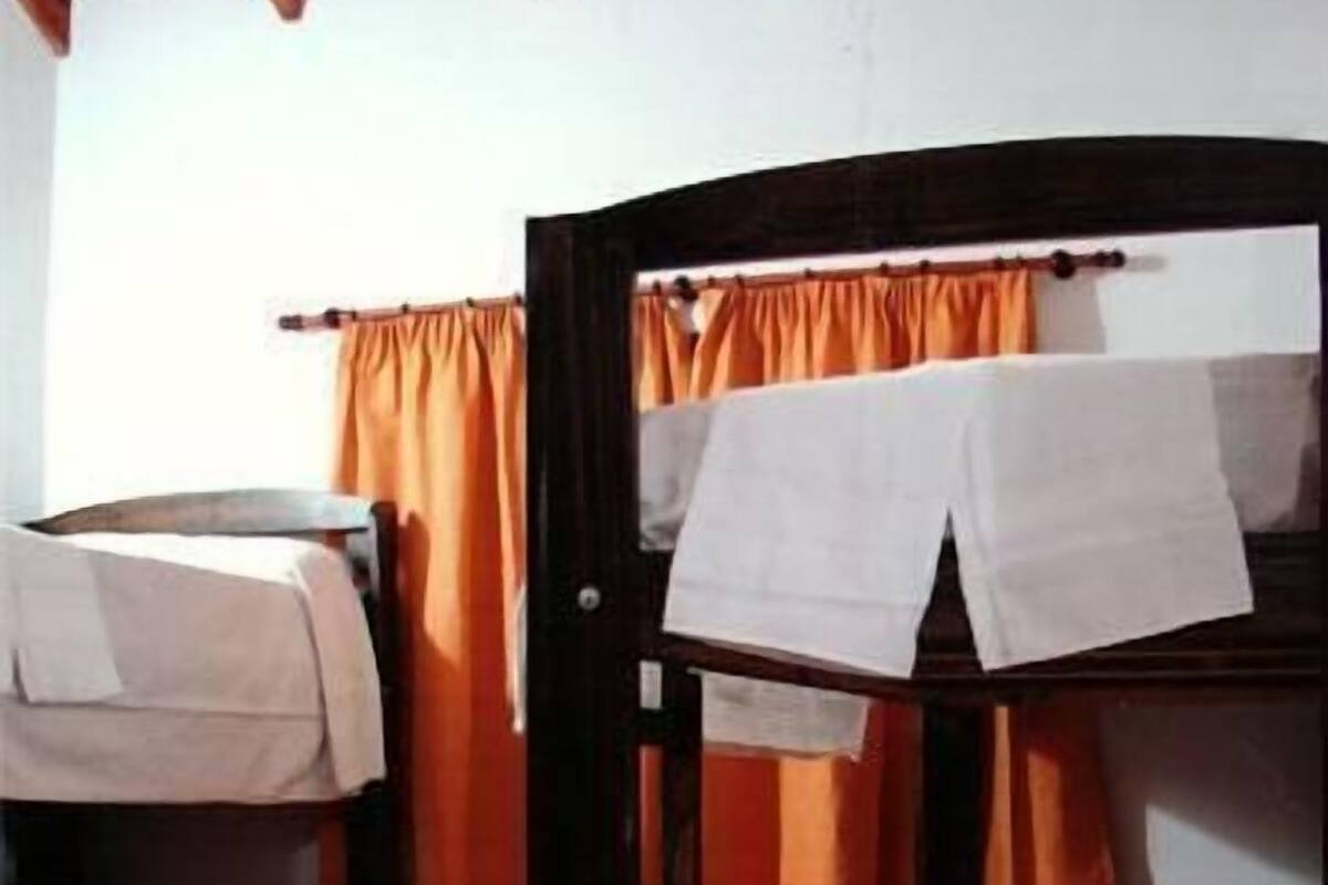 Une chambre avec un lit superposé, des rideaux orange et du linge de lit blanc.