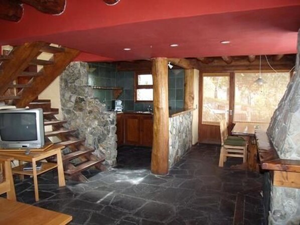 A rustic interior with a stone fireplace, wooden staircase, and a dining area. - Marinas Alto Manzano (Villa La Angostura)