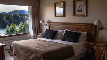 Una habitación de hotel con una cama, dos mesitas de noche, una lámpara y vistas a un lago y montañas.