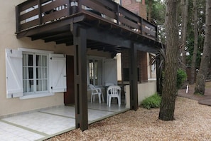 Un espacio al aire libre cubierto con una mesa, sillas, una pérgola y un edificio con ventanas y una puerta.