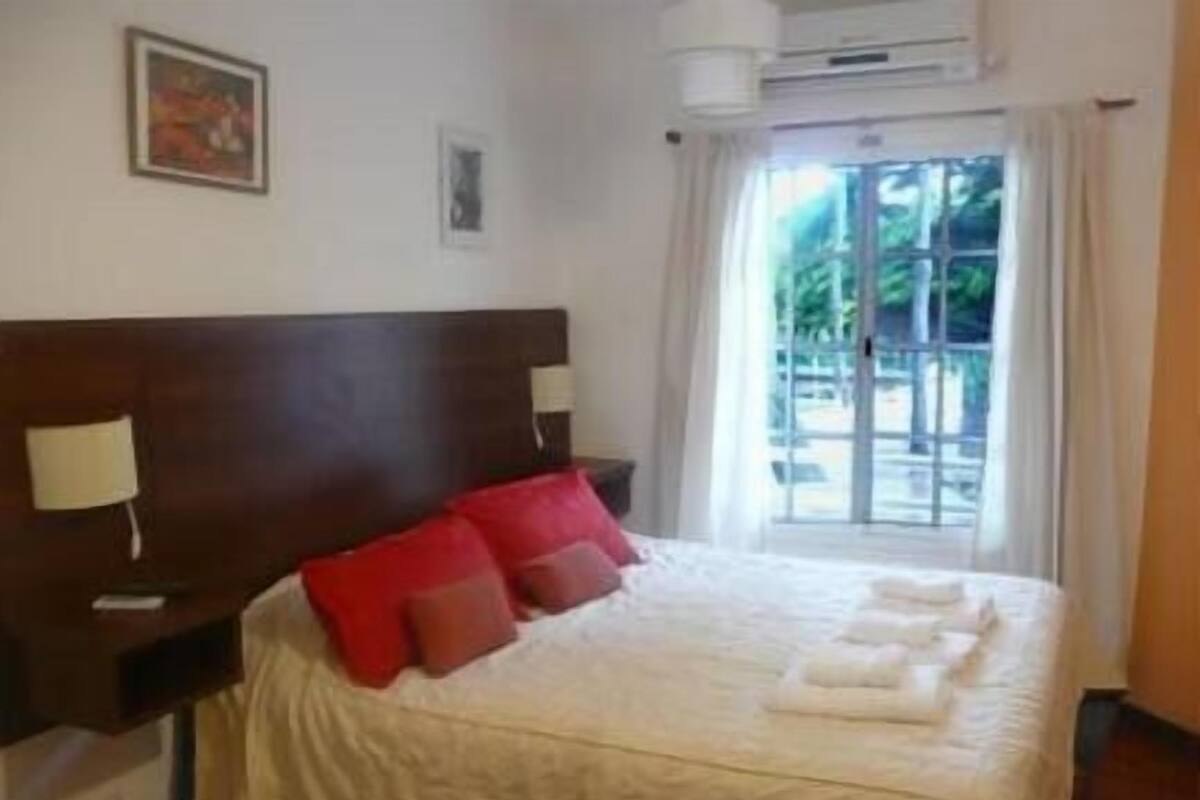 Une chambre d’hôtel avec un grand lit, une tête de lit en bois, une fenêtre avec des rideaux et un tableau au mur.