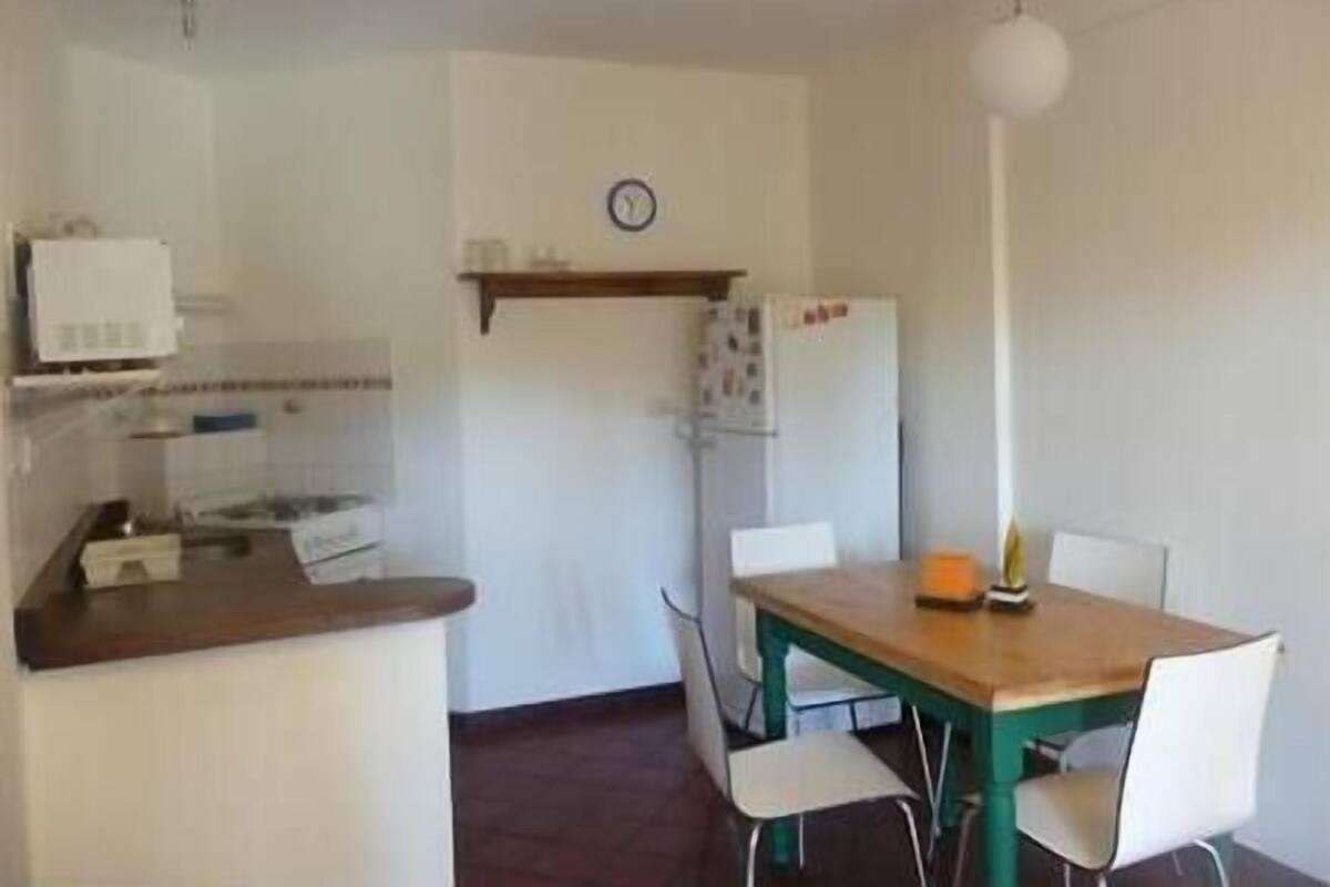 Une cuisine de taille réduite avec un plan de travail en bois, un réfrigérateur blanc, une horloge au mur et une table à manger avec des chaises.