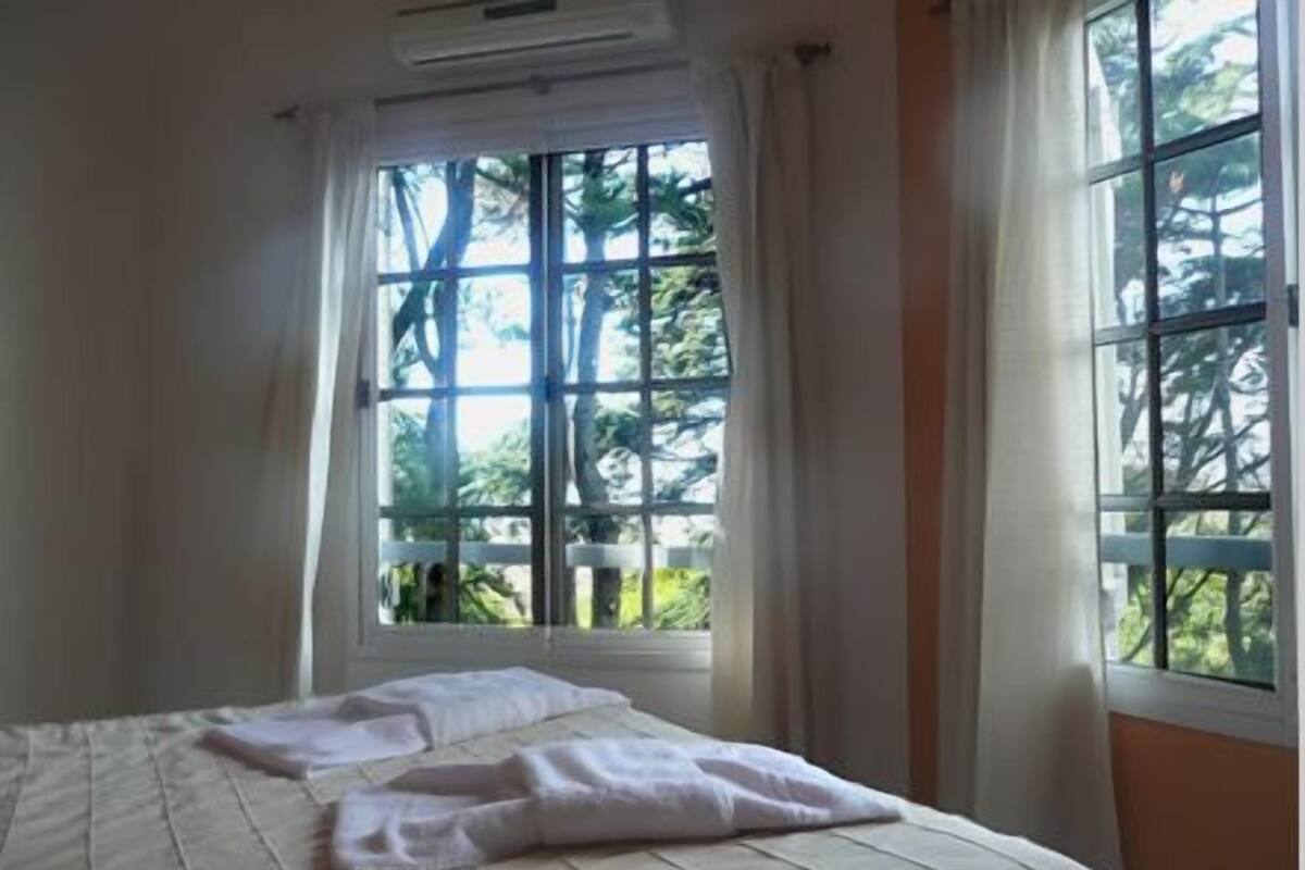 Une chambre à coucher avec un lit, une fenêtre avec des rideaux et une vue sur les arbres à l’extérieur.