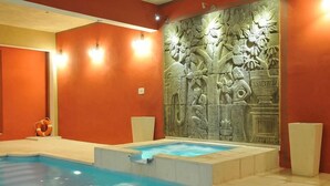 Une piscine bordée d’un mur en pierre orné de sculptures, entourée de murs orange et agrémentée de deux luminaires.