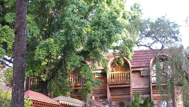 Un bâtiment traditionnel doté de nombreux balcons, entouré d’une végétation luxuriante et agrémenté d’un jardin bien entretenu.