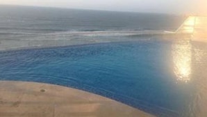 Piscina com borda curva e vista para o oceano.