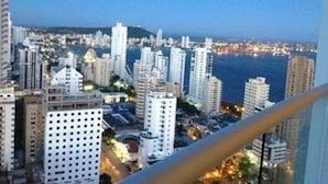 Paisagem urbana com arranha-céus, céu claro e um corpo de água ao longe.