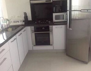 A compact kitchen with white cabinets, a black countertop, a microwave, a stove, and a refrigerator. - Palmetto Eliptic Apartamentos (Cartagena de Indias)
