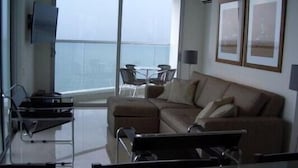 Uma sala de estar moderna com uma mesa de centro de vidro, um sofá e uma TV fixada na parede.