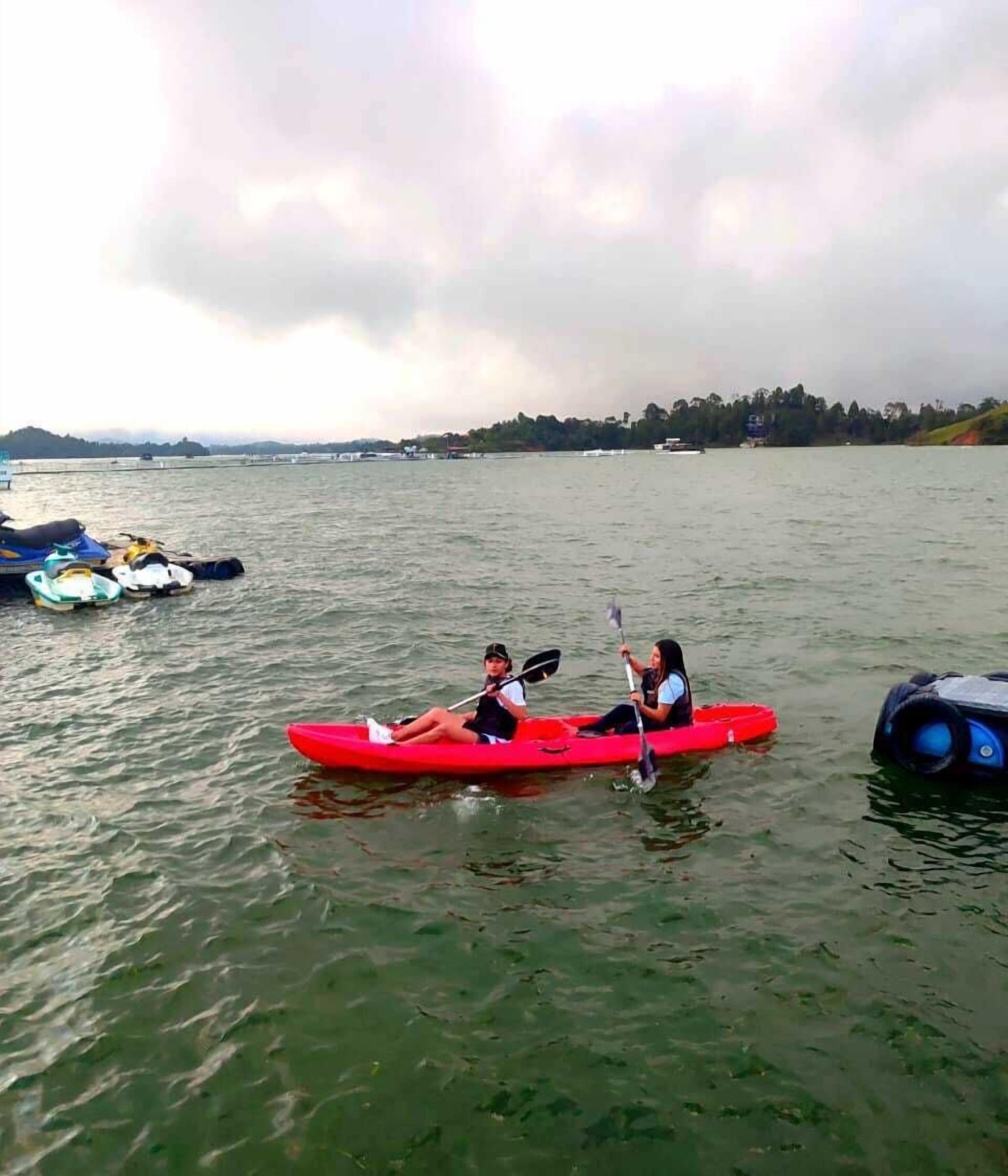 A calm lake with a red kayak in the center, surrounded by calm water and a cloudy sky.