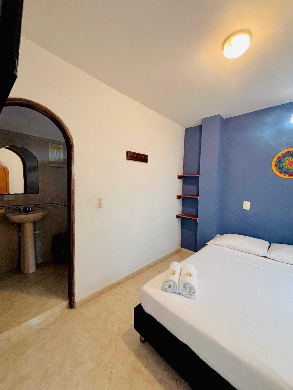 A hotel room with a bed, a small bathroom with a sink, and a blue accent wall.