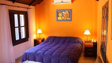 A bedroom with a large bed, two bedside tables with lamps, a wall-mounted air conditioner, and a window with curtains.