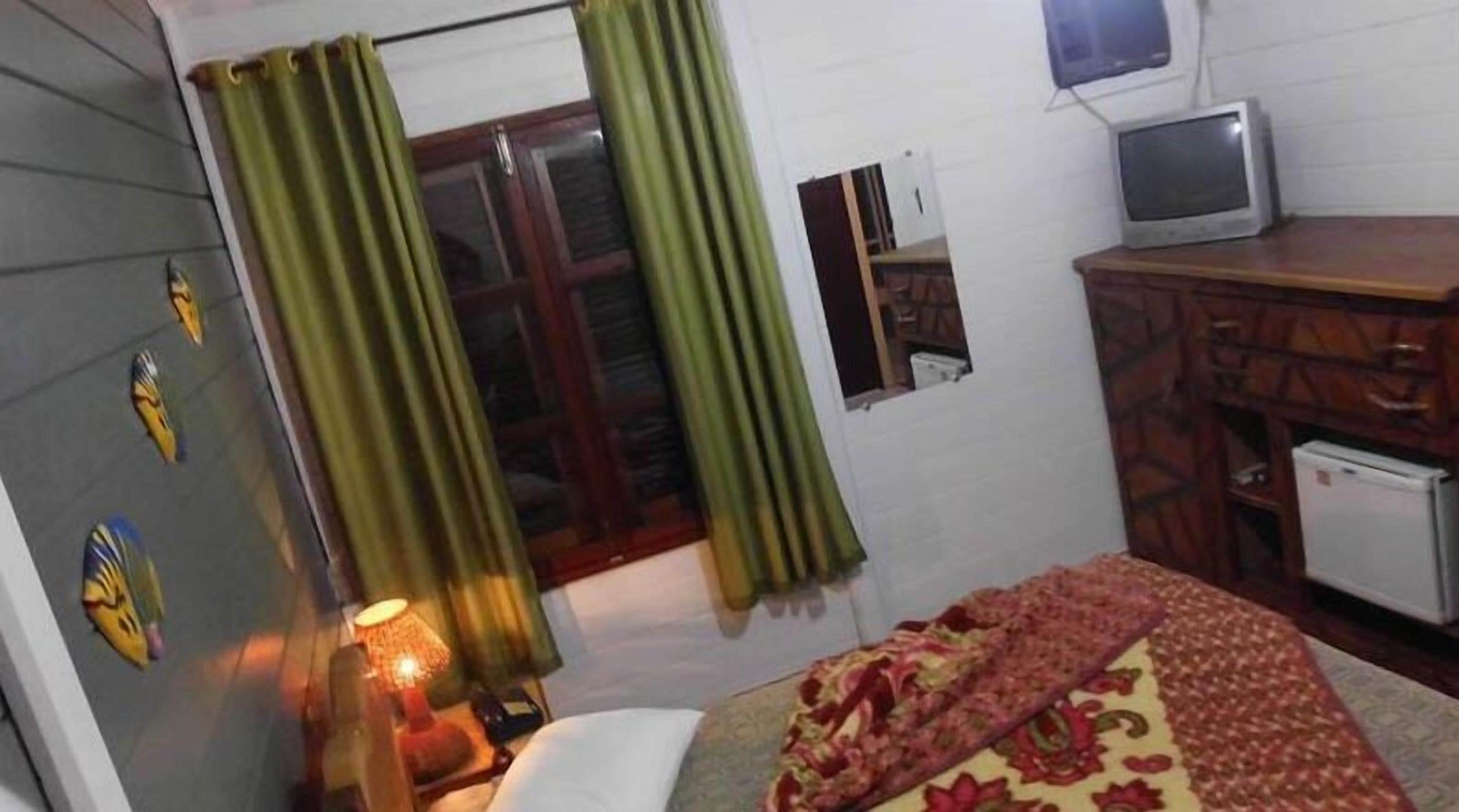 Una habitación con cama, una mesita, televisor y ventana con cortinas.
