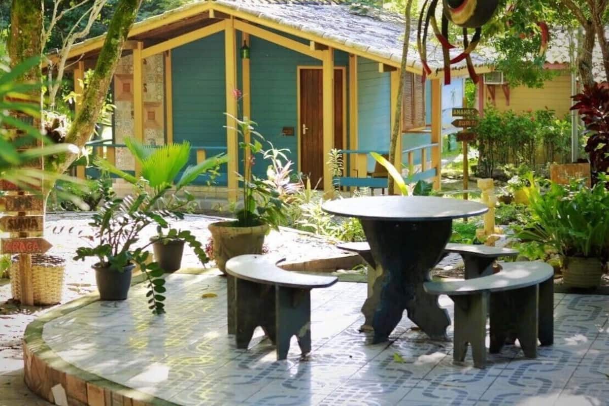 A rustic wooden house with a green door and a tiled patio area with a round table and four chairs.