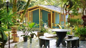A rustic wooden building with a tiled patio area, surrounded by lush greenery and potted plants.