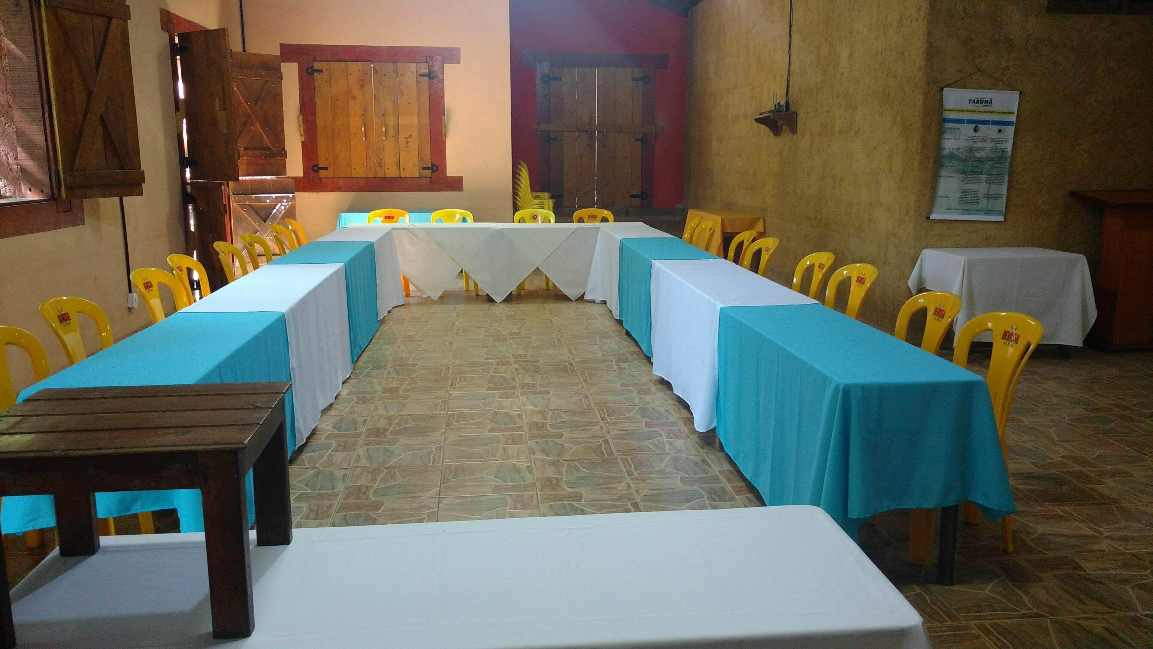 A long table with blue tablecloths and yellow chairs in a room with stone flooring and wooden doors.