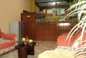Una zona de recepció amb un taulell de fusta, un refrigerador i un sofà amb un disseny floral.