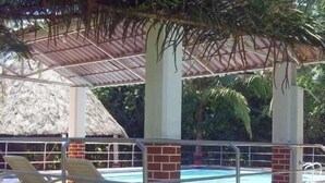 A covered pool area with lounge chairs and a thatched-roof structure in the background. - Finca 028 (Restrepo)