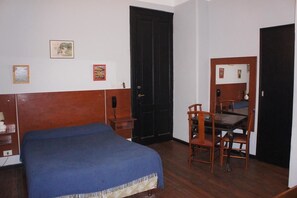 Une chambre à coucher avec un lit, une commode en bois, un bureau avec une chaise et une porte noire.