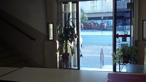 A view from a window with a staircase leading down, a potted plant, and a view of a street with parked cars and a building in the background. - Gran Hotel America (Buenos Aires)