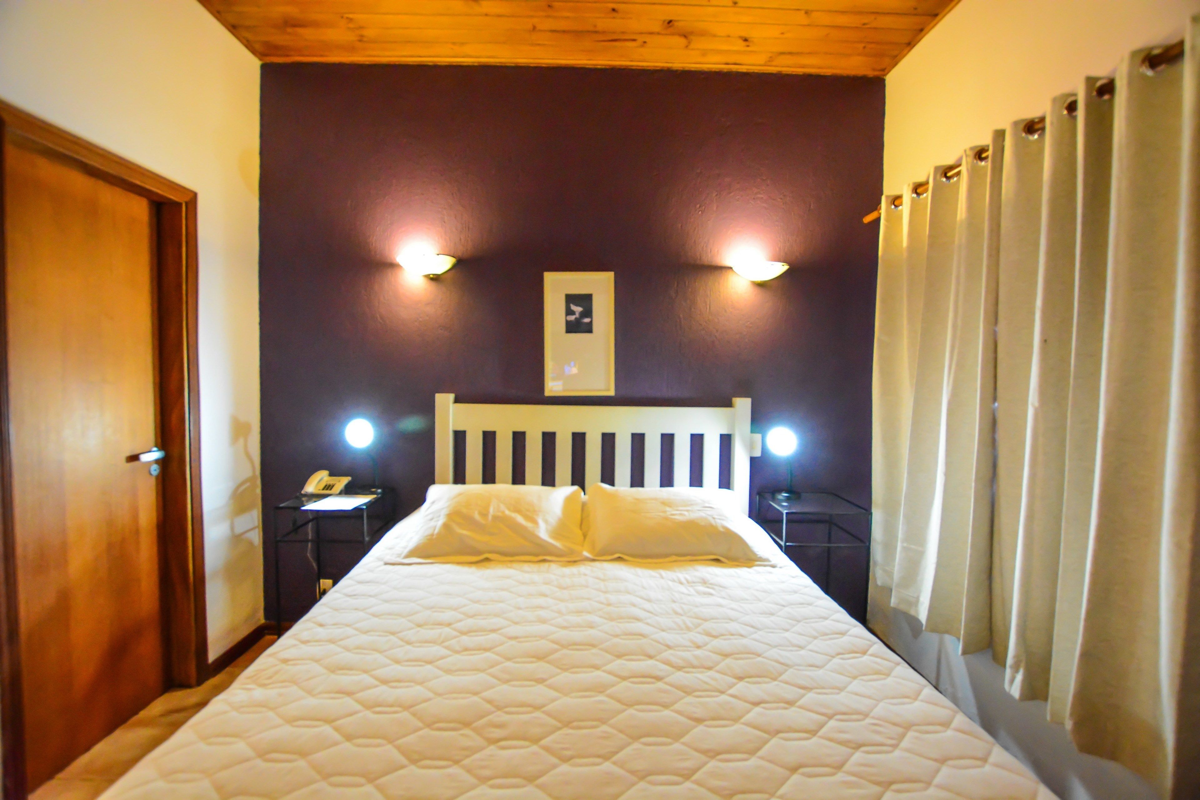 Une chambre à coucher avec un lit, une tête de lit en bois, deux tables de chevet avec des lampes, une porte et un rideau.