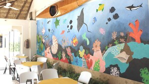 A restaurant with a mural of marine life on the wall, white chairs, and yellow tablecloths. - Hotel Arrecife Plus (Santa María Huatulco)