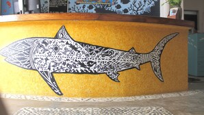 A reception desk with a shark mural, a welcome sign, and a plant. - Hotel Arrecife Plus (Santa María Huatulco)
