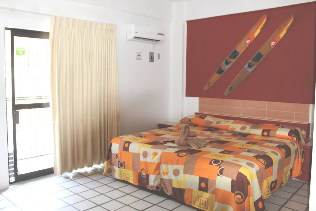 A hotel room with a bed, curtains, an air conditioning unit, and a ski-themed wall decoration.