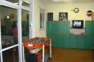 Una habitación con mesa de fútbol, televisor y muebles verdes.