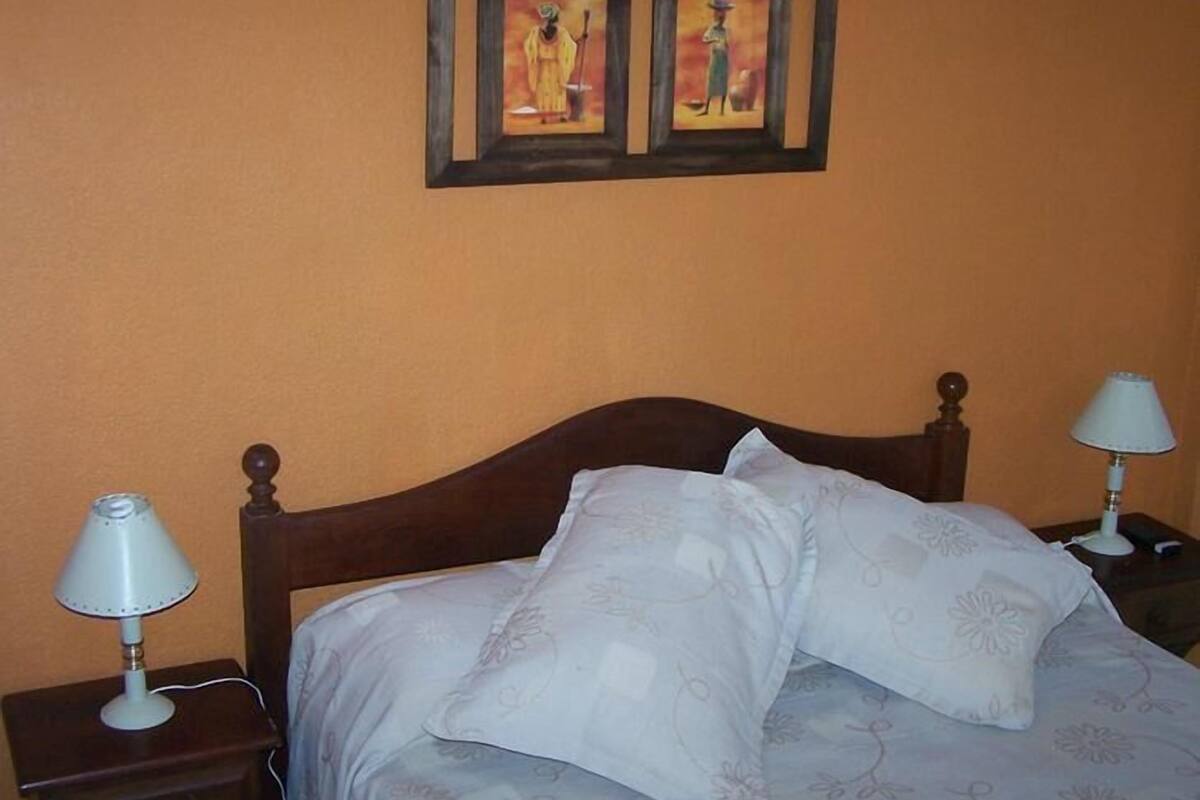 A bedroom with a wooden bed, two bedside lamps, and two framed paintings on the wall.