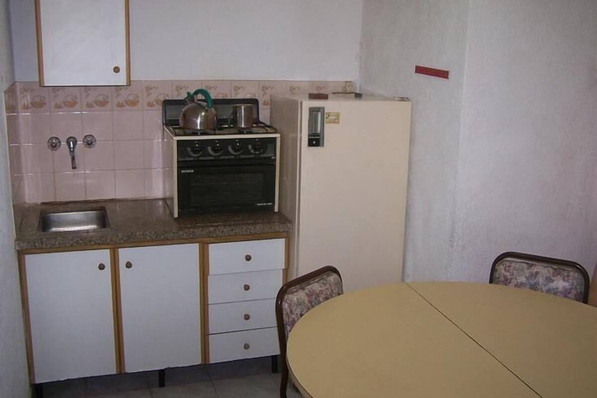 A compact kitchen with a stove, sink, and a refrigerator. There is a dining table with chairs.