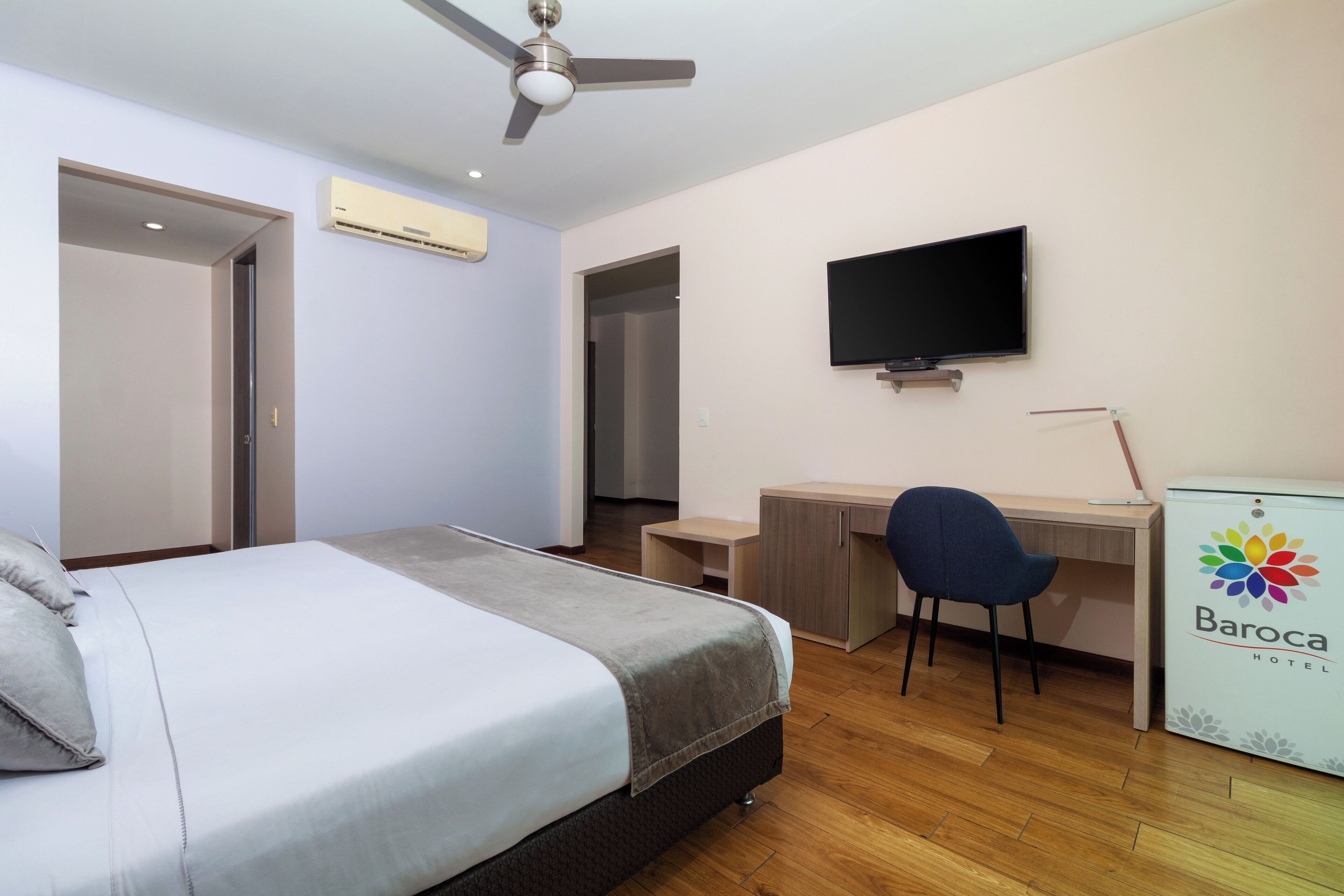 A hotel room with a bed, a desk, a chair, a television, and an air conditioning unit.