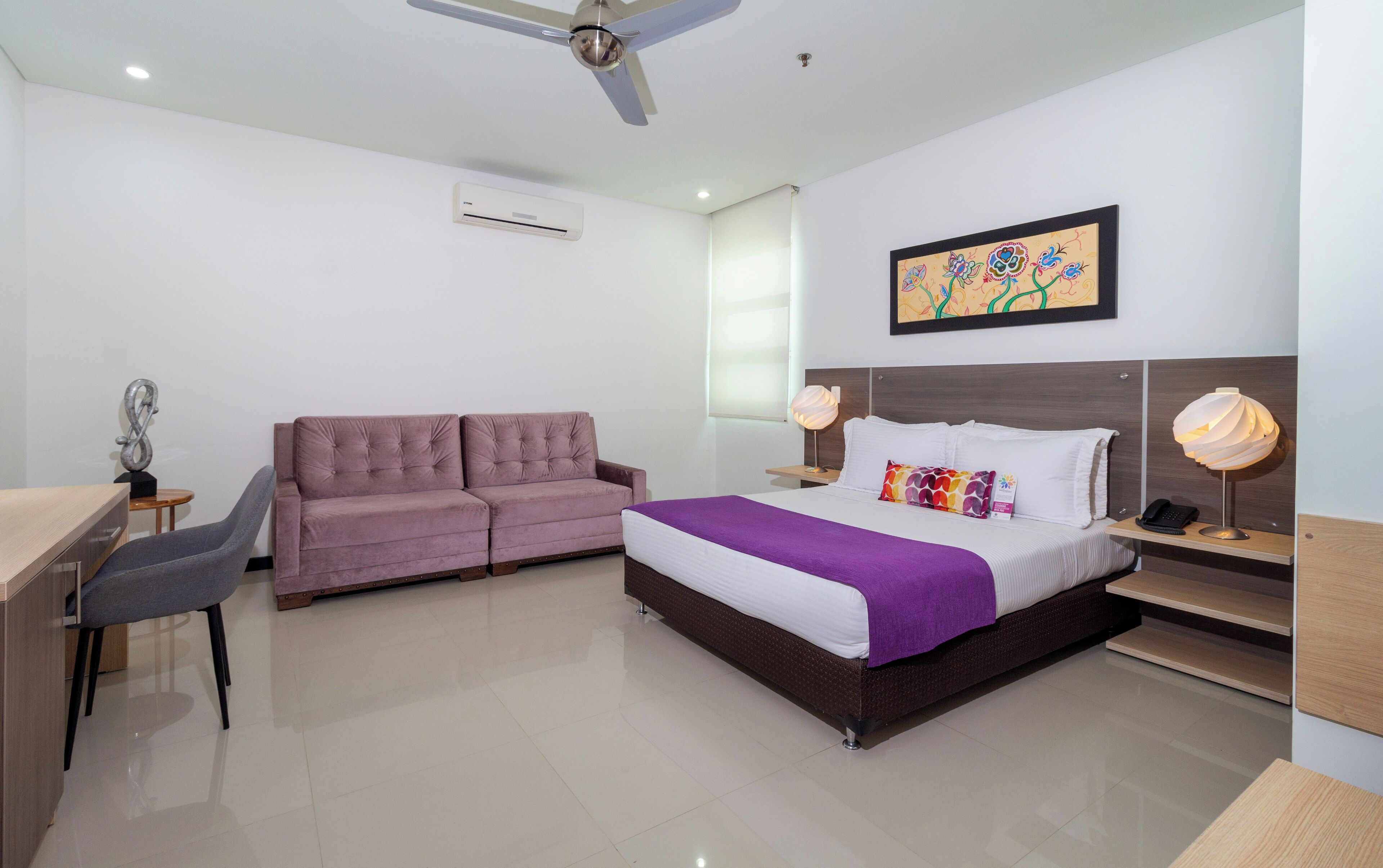 A modern hotel room with a bed, a sofa, a desk, and a chair.